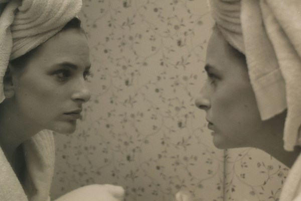 Black and white profile photo of actress Marlee Matlin wearing a towel on her head and bathrobe looking intently into a mirror.