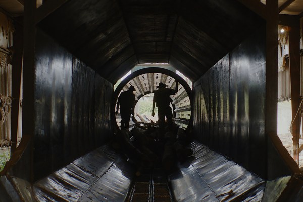 Two silhouetted workers standing inside a large industrial chute at a paper mill