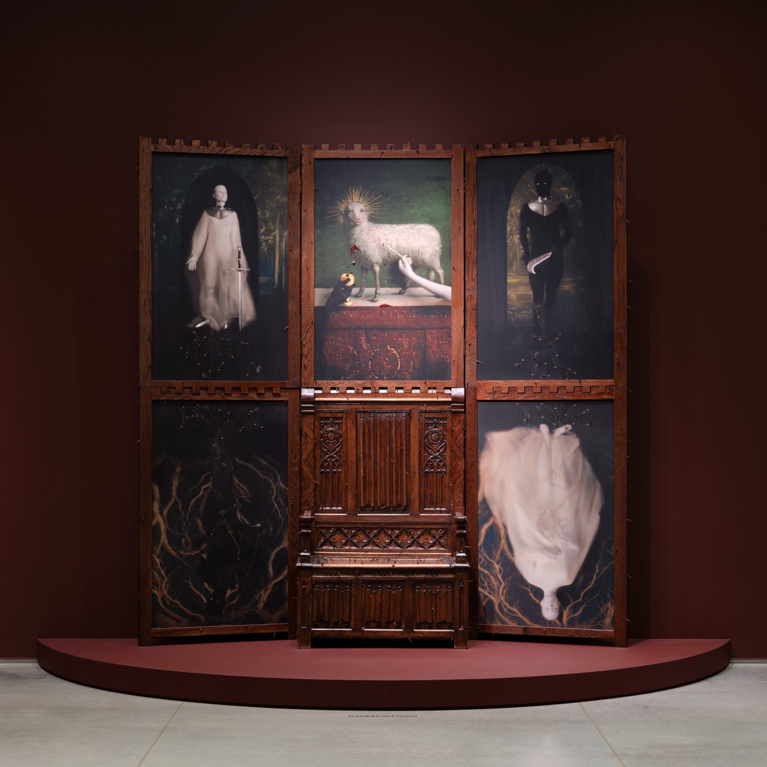 A six-panel artwork in dark wood frames, arranged in two rows of three. The top row features three paintings: a white-robed figure with a sword, a lamb with a halo and a chalice, and a dark figure holding a dagger. The bottom row has two paintings depicting golden root-like patterns and inverted figures in black and white, flanking a richly carved wooden structure.