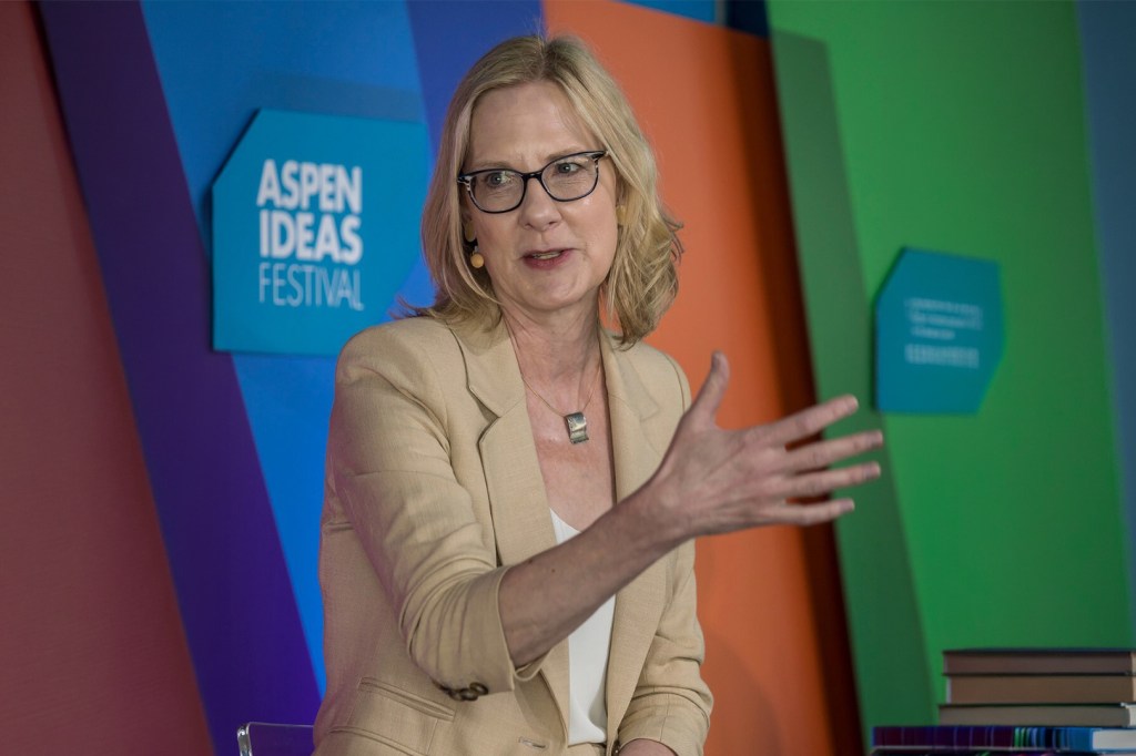 Heather Gerken wearing glasses and a beige blazer gestures while speaking on stage in front of a colorful backdrop featuring the "Aspen Ideas Festival" sign, highlighting leadership discourse at the 2026 Aspen Ideas Festival event.