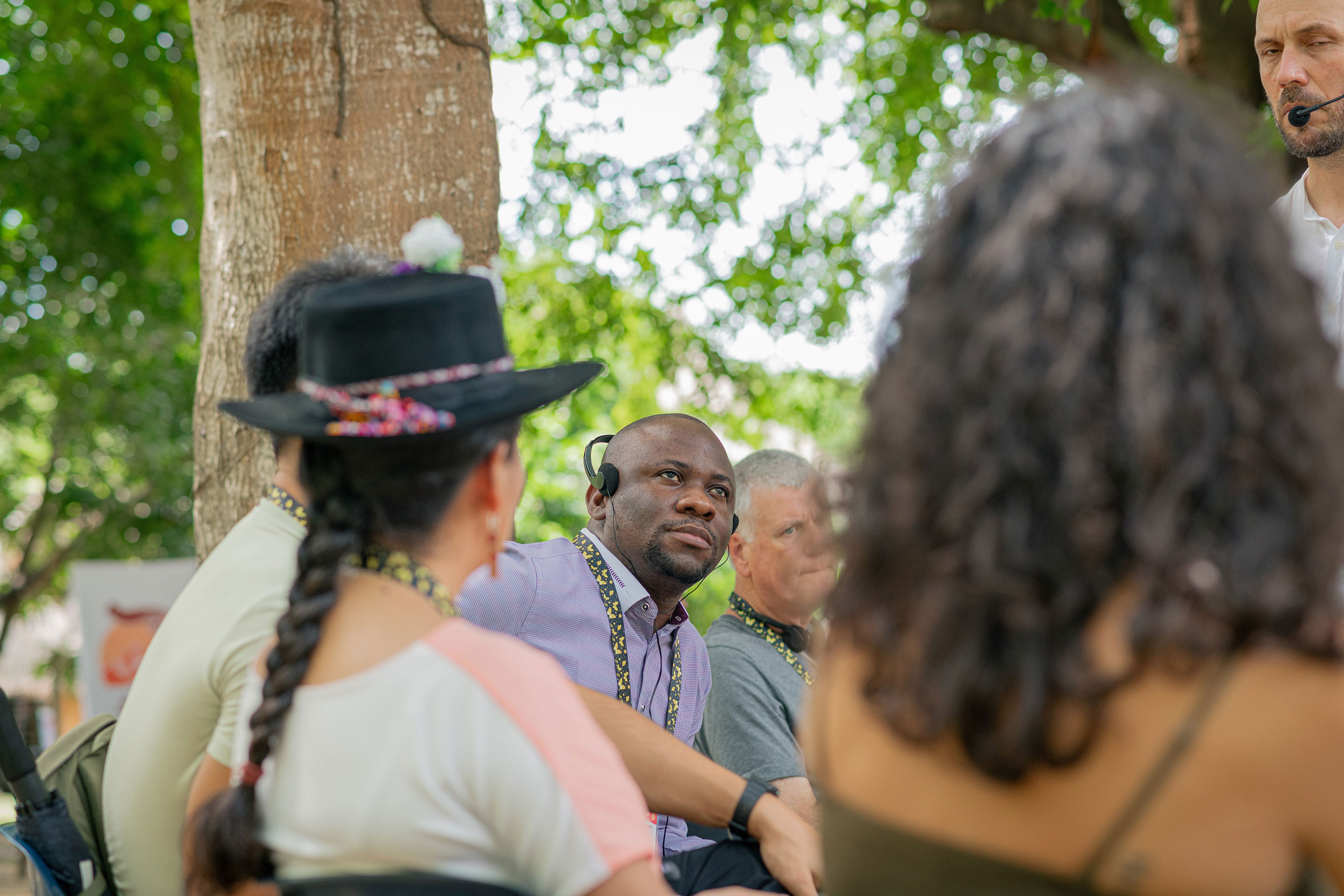 Rasak Adekoya wearing a translation headset and listening attentively during an outdoor group discussion on disability inclusion systems.