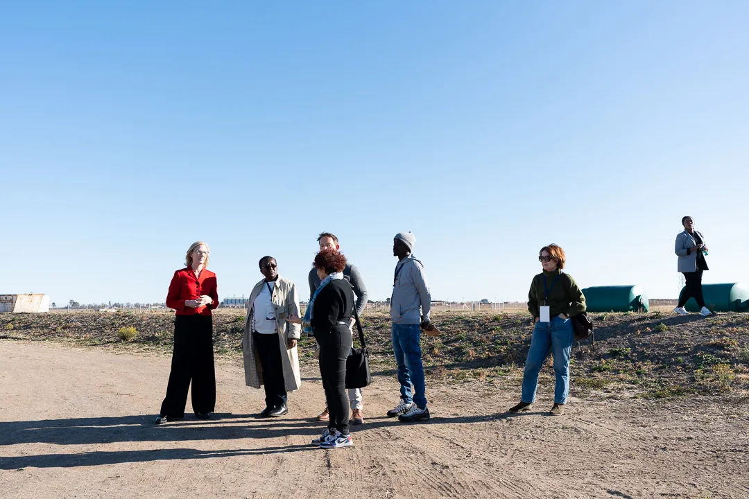 A delegation of organizational leaders standing outdoors on a dirt path under a clear blue sky during a site visit in South Africa.