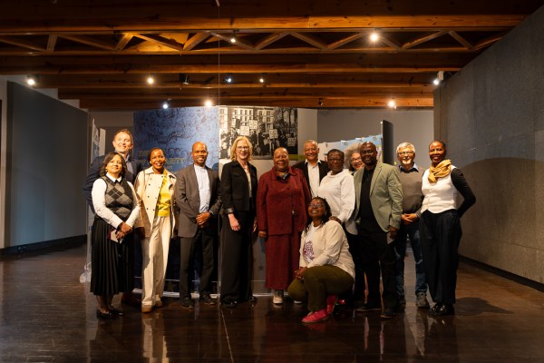 A group of diverse leaders and delegates pose together inside a museum hall featuring historical exhibition banners, taken during a visit to South Africa.