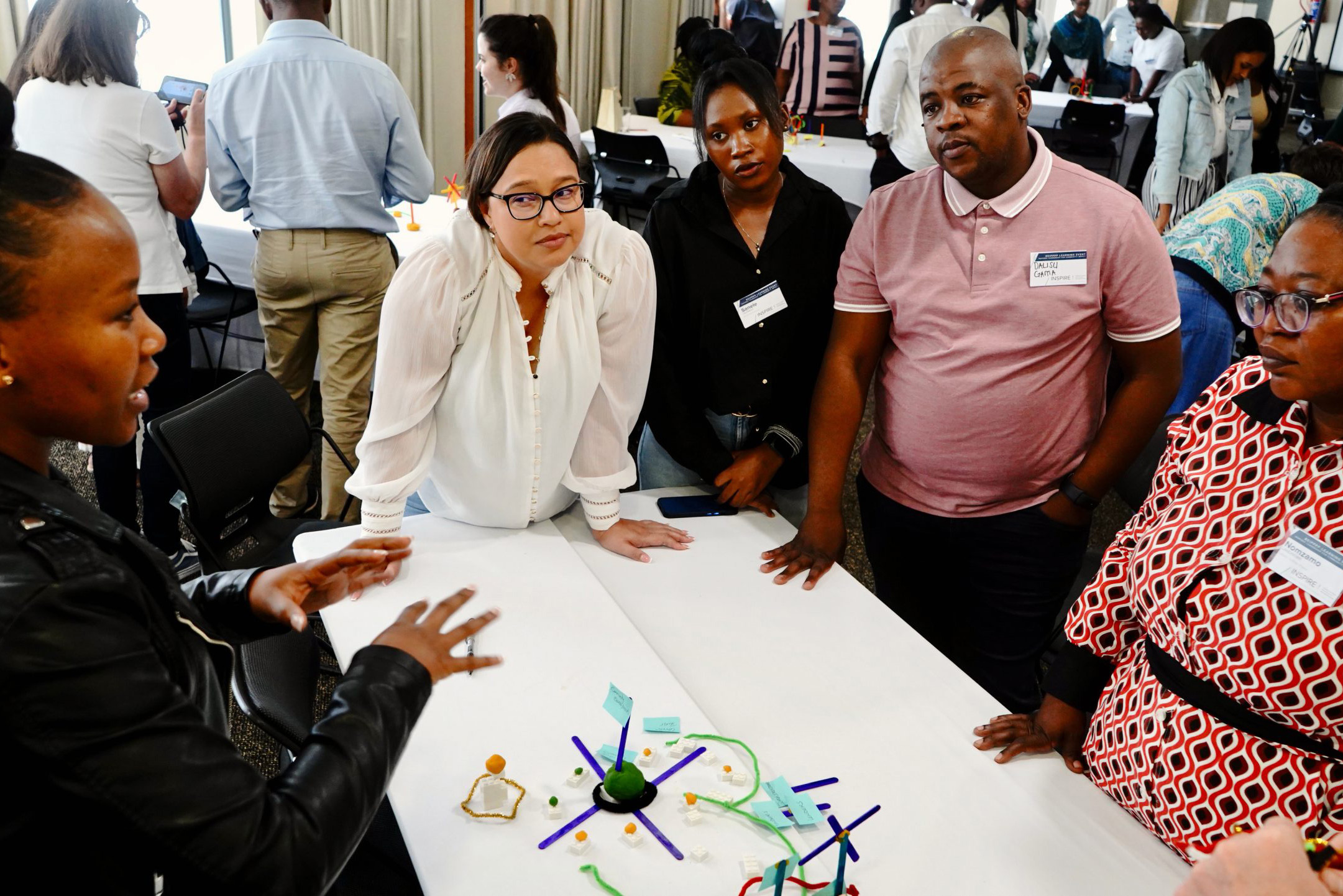 A group of community trust members leaning over a table, listening attentively as a speaker gestures near a 3D model, representing South Africa’s energy transition collaboration.
