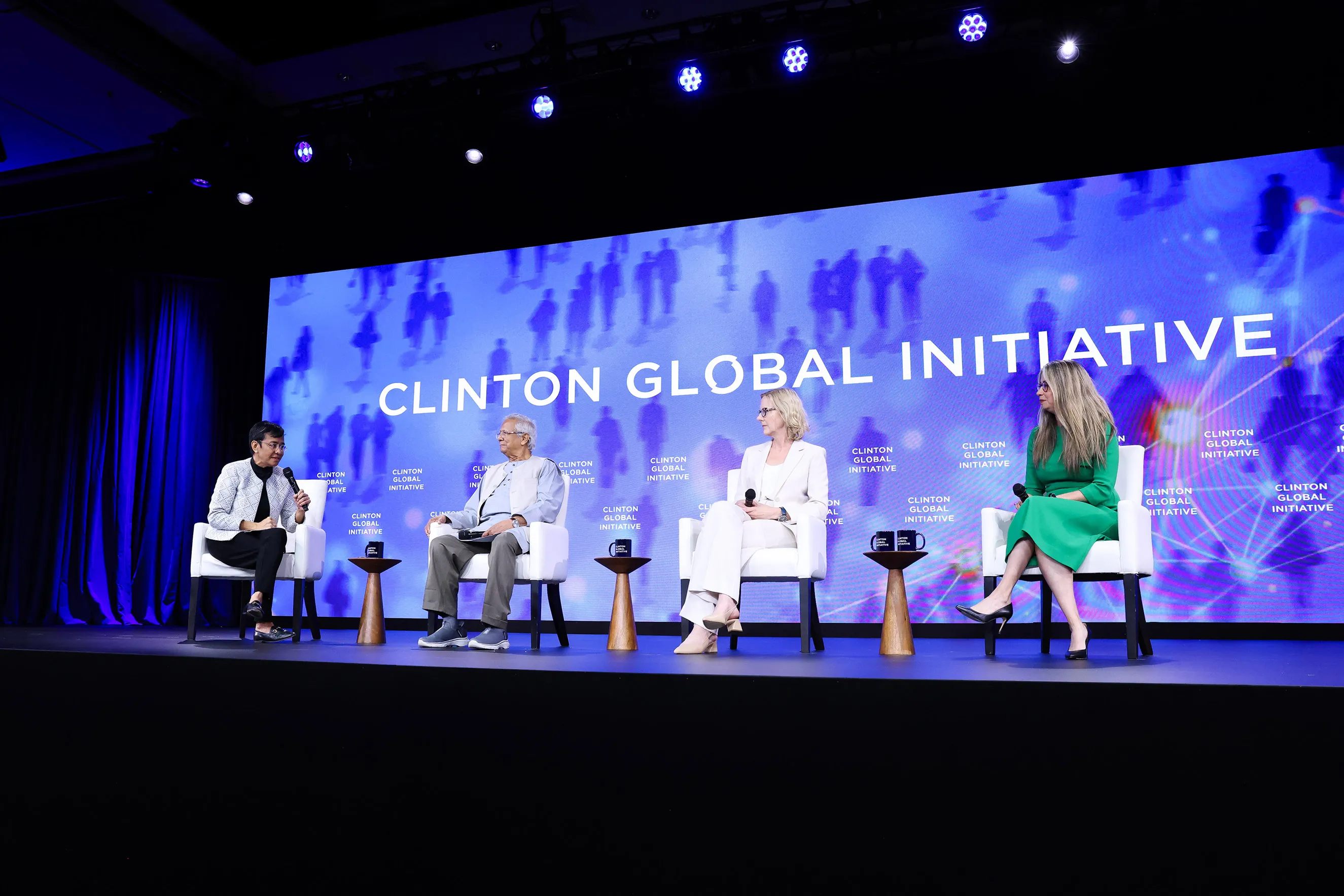 Four panelists seated on stage during a discussion at the Clinton Global Initiative, with a large blue background screen displaying the event title behind them.